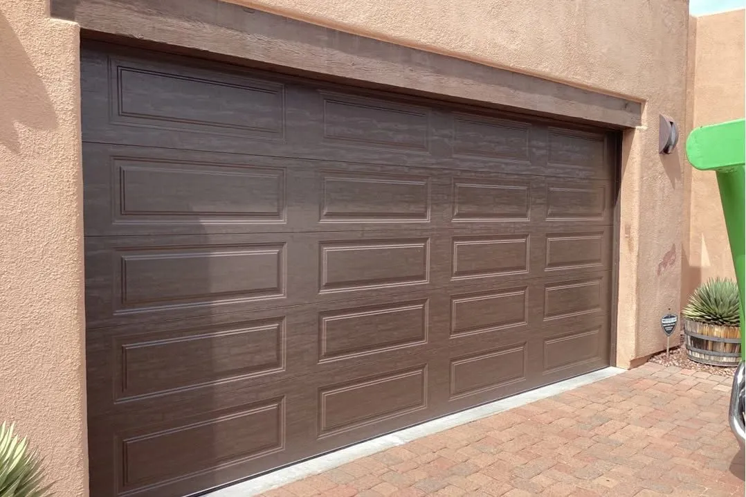 Brown raised-panel garage door on a southwestern stucco home with a paver driveway