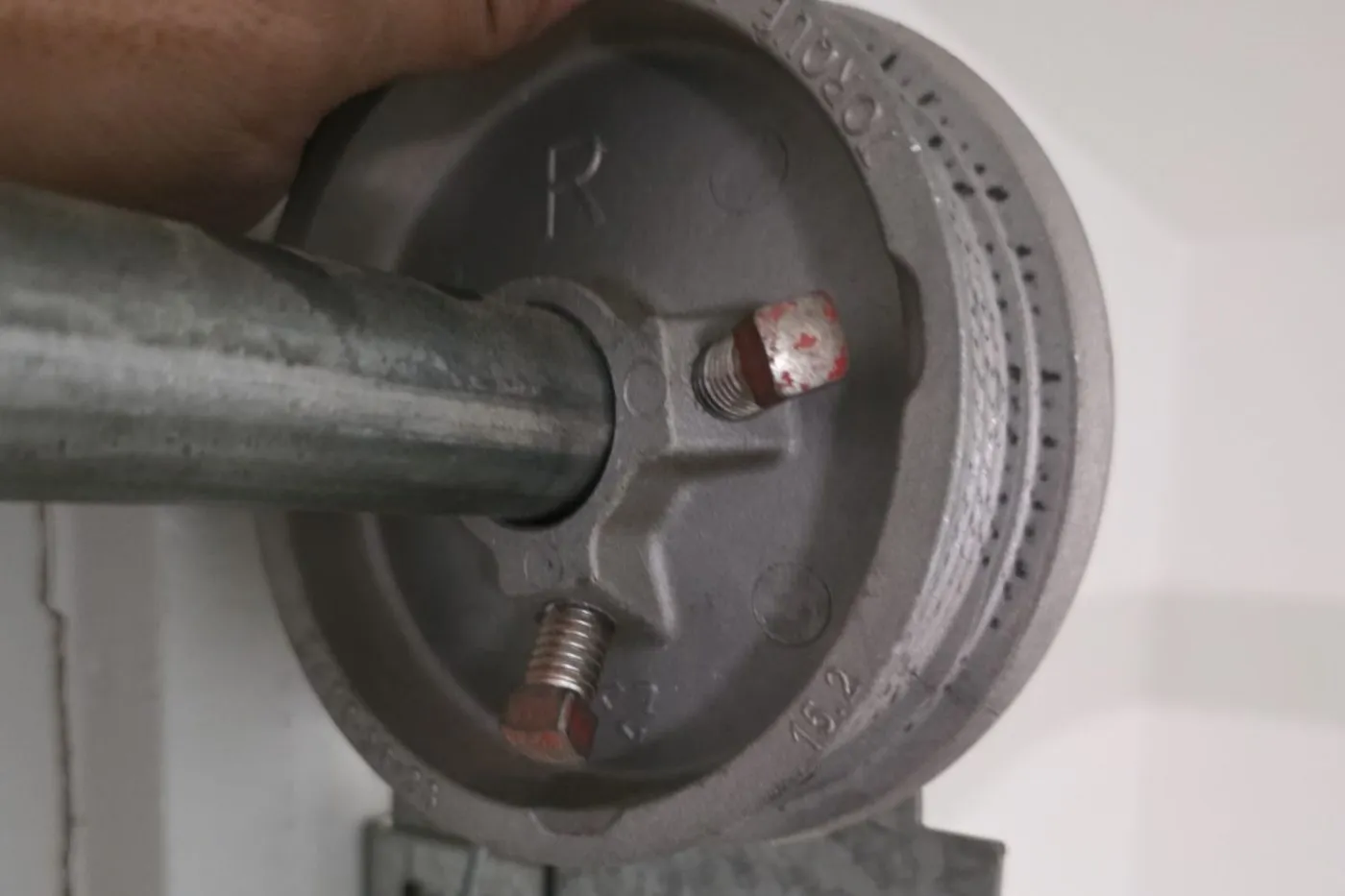 Hand holding a cable drum on the torsion shaft above a garage door