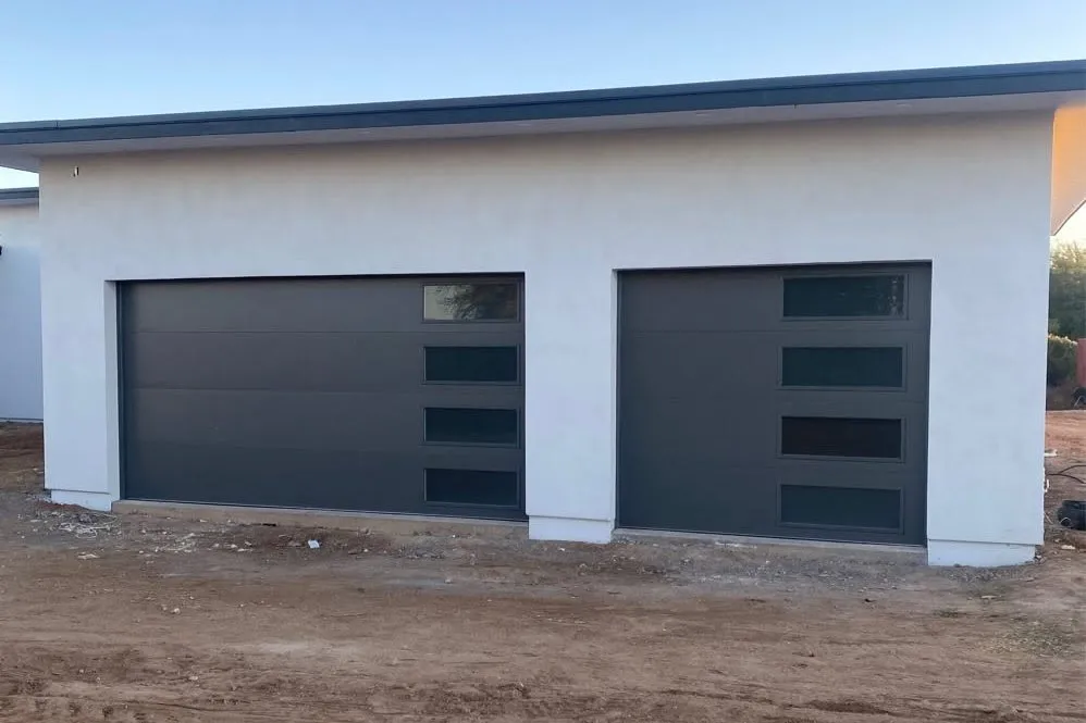 Two charcoal garage doors with narrow windows on a new stucco home