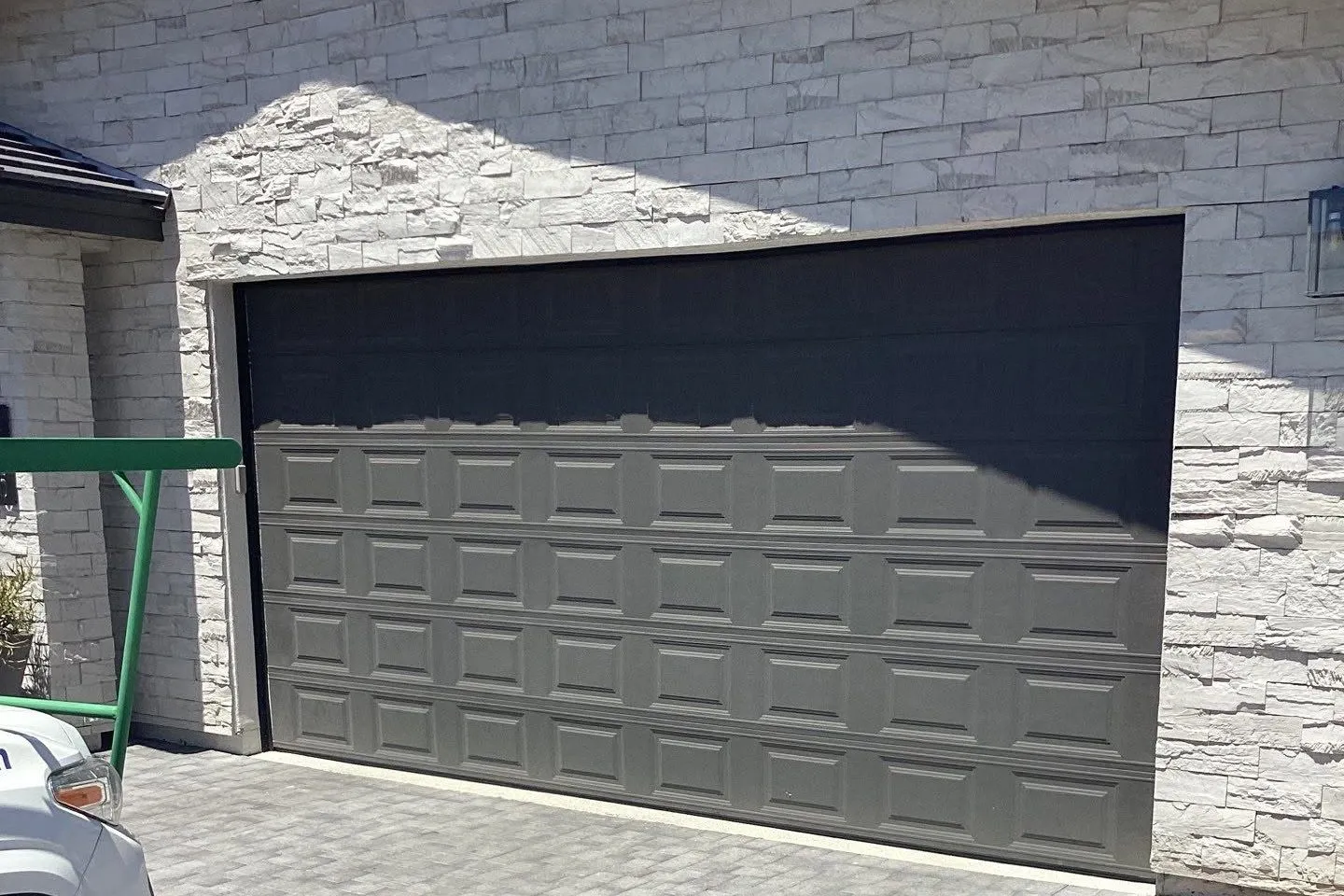 Dark charcoal garage door on a stone-faced home with a gray paver driveway