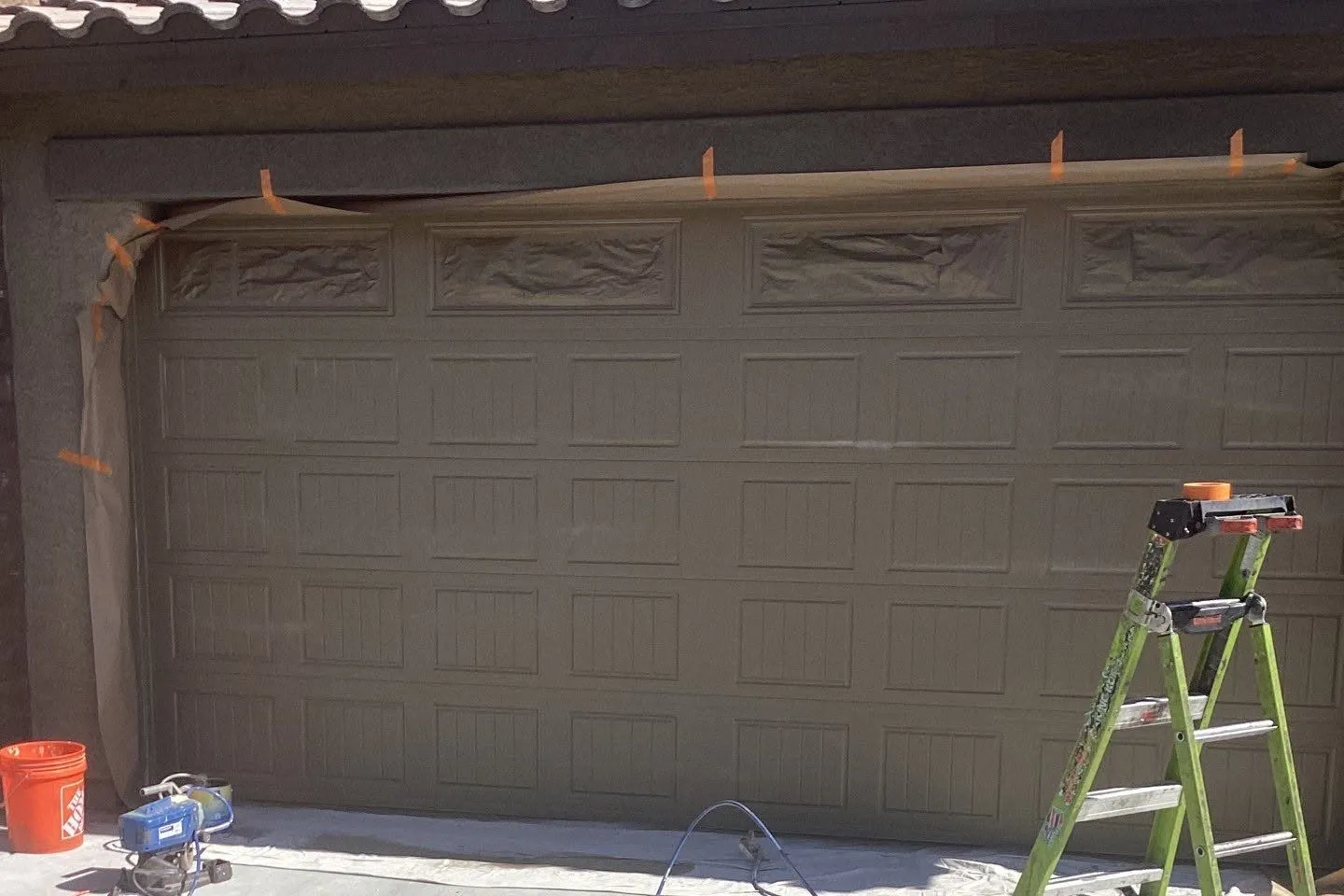 Garage door being prepped for paint with a sprayer and ladder on the driveway