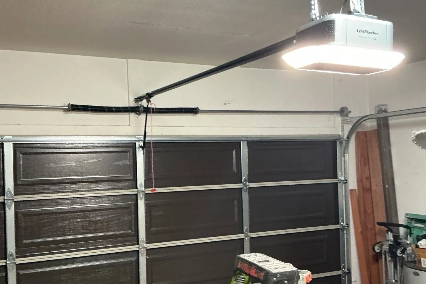 Sectional garage door with the opener rail overhead and a ladder in the garage during a repair visit