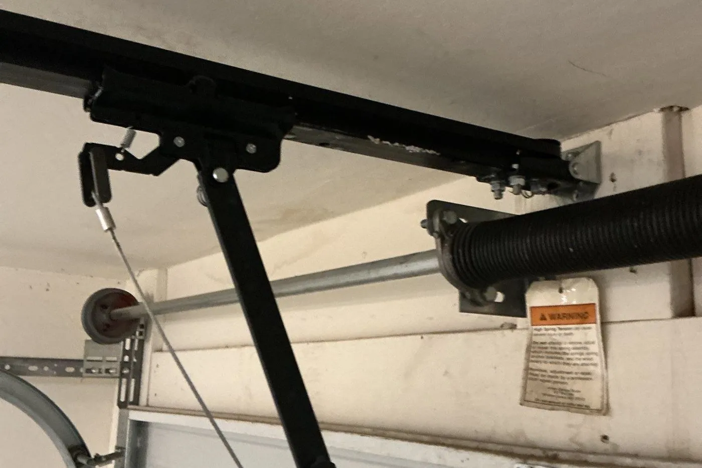 Torsion spring, cable and opener arm above a sectional garage door