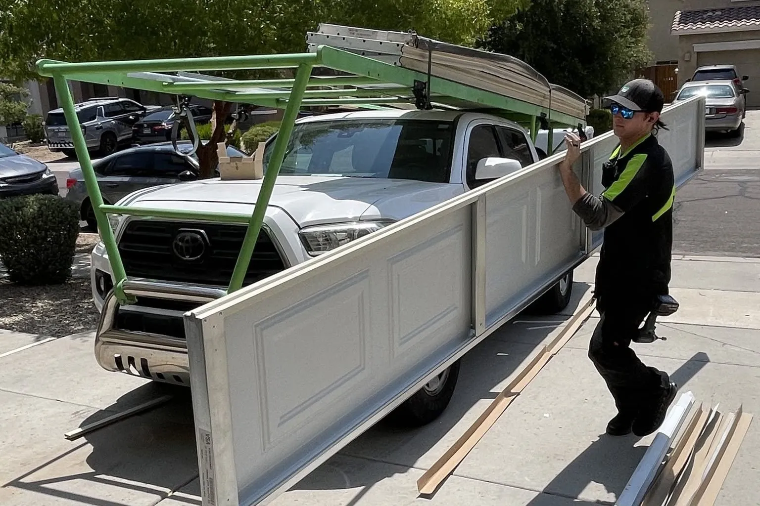 Technician carrying a new garage door panel beside a truck with a door rack