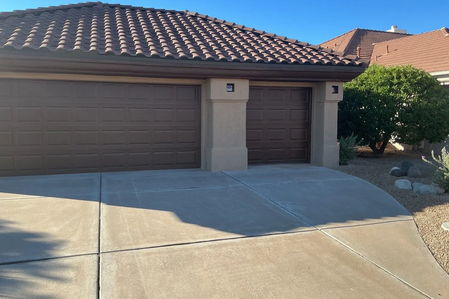 Three-car garage with brown raised-panel doors under a tile roof and a curved concrete driveway
